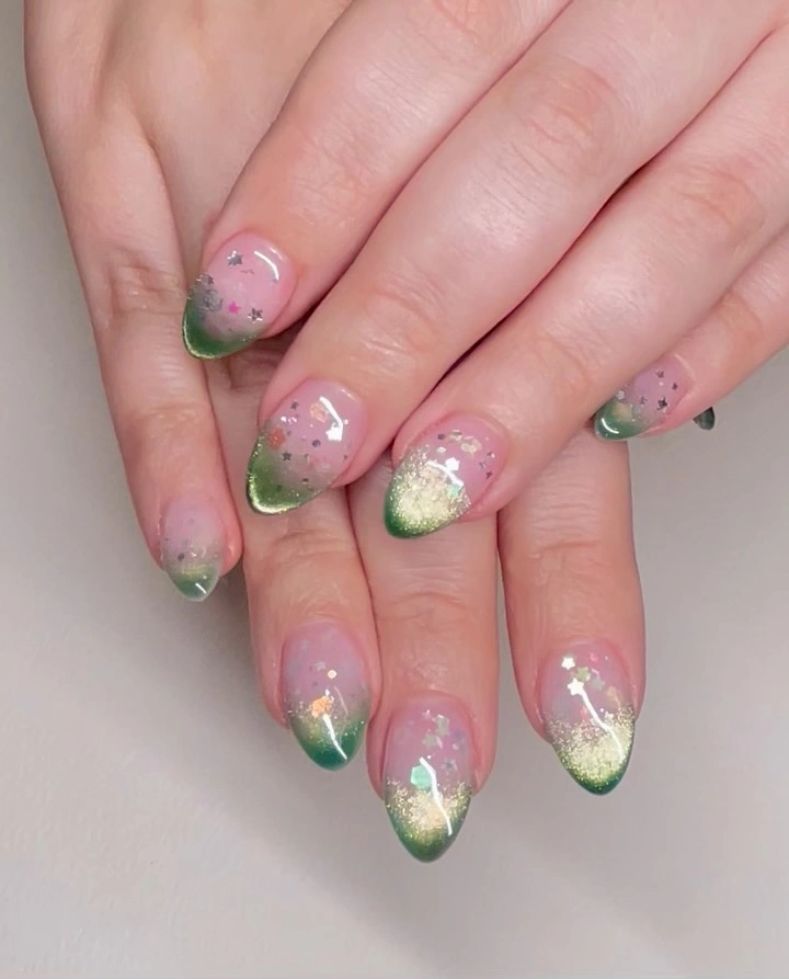 Pink almond nails with green shimmering tips and scattered tiny stars