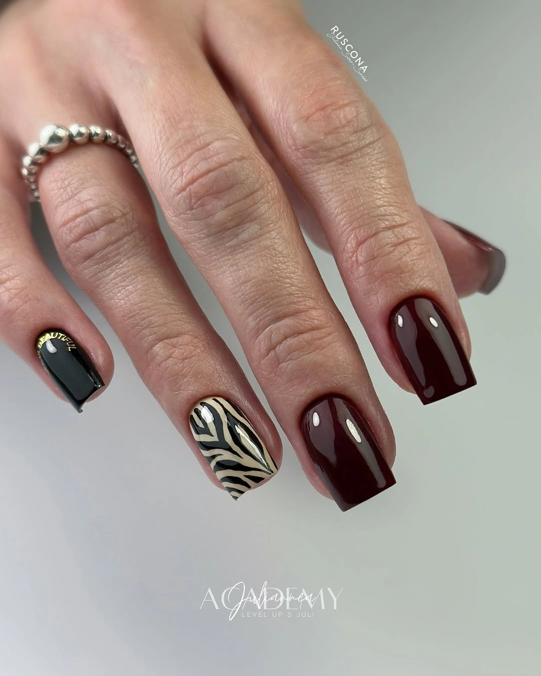 Glossy burgundy square nails with black accents and cream zebra pattern
