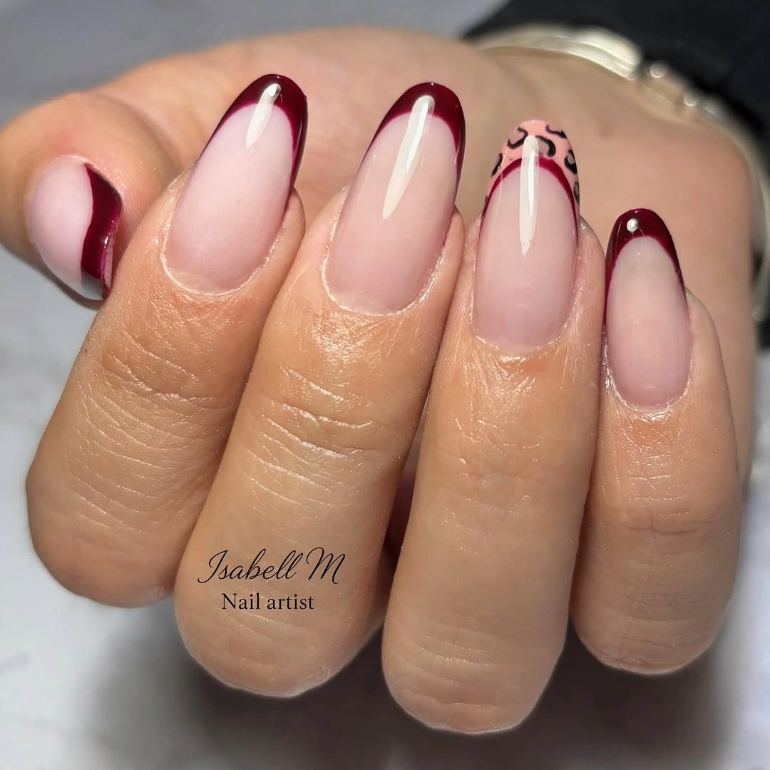 Pale pink almond nails with burgundy French tips and one leopard-patterned tip