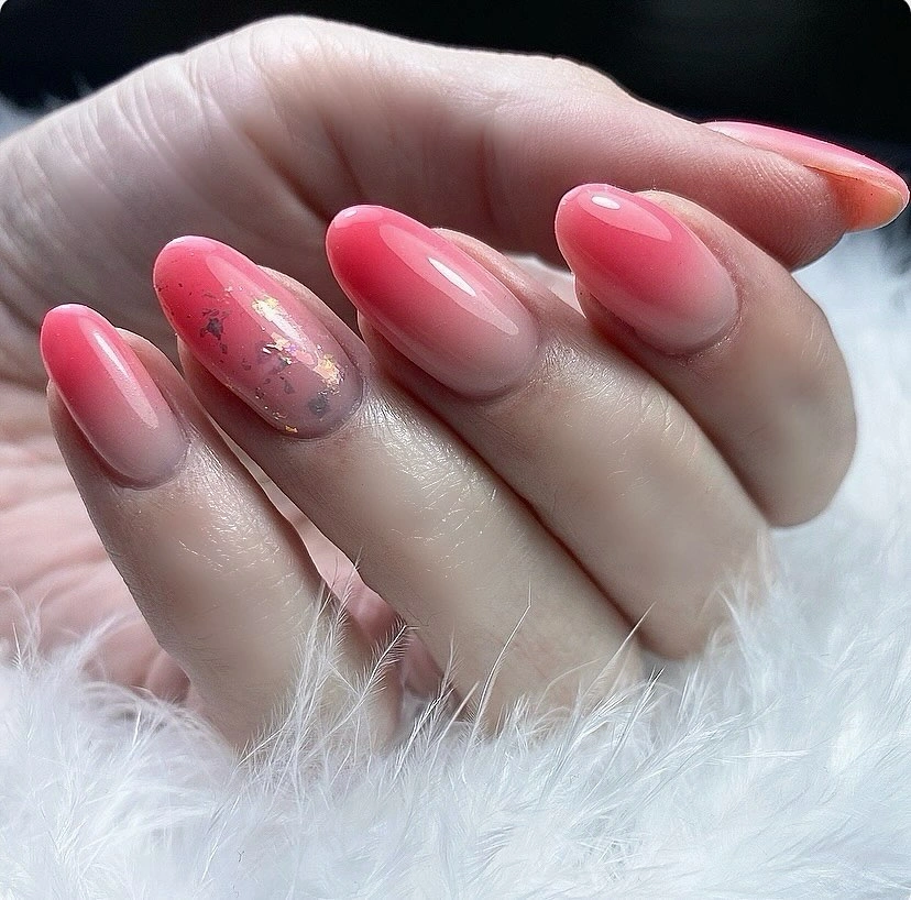 Rounded almond nails with coral pink gradients and one reflective accent