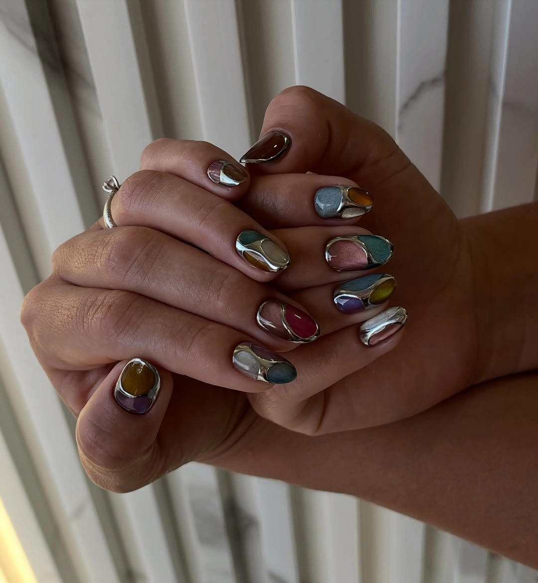 Short rounded nails with burgundy teal mustard and lavender sections edged in silver