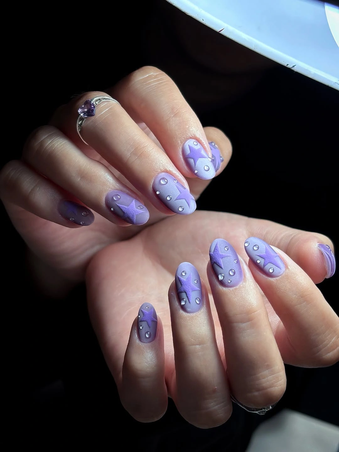 Short lavender nails decorated with purple stars and small silver colored dots