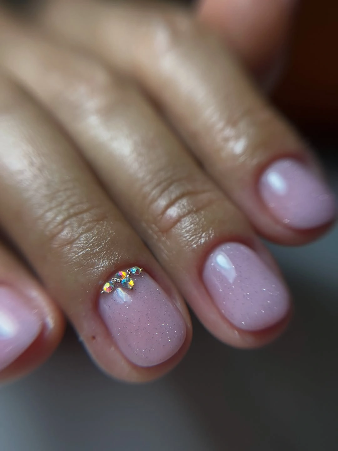 Short rounded pale pink nails with fine sparkle and iridescent cuticle accents